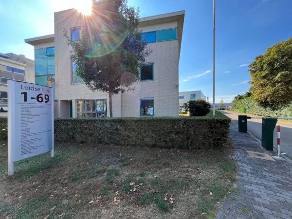 Kantoorpand in Leidse Rijn met zonlicht dat door een boom schijnt en een bord met huisnummers 1-69 op de voorgrond.